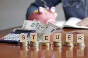Steuern beim Auswandern als Selbstständiger — Taschenrechner, Münzen und Sparschwein