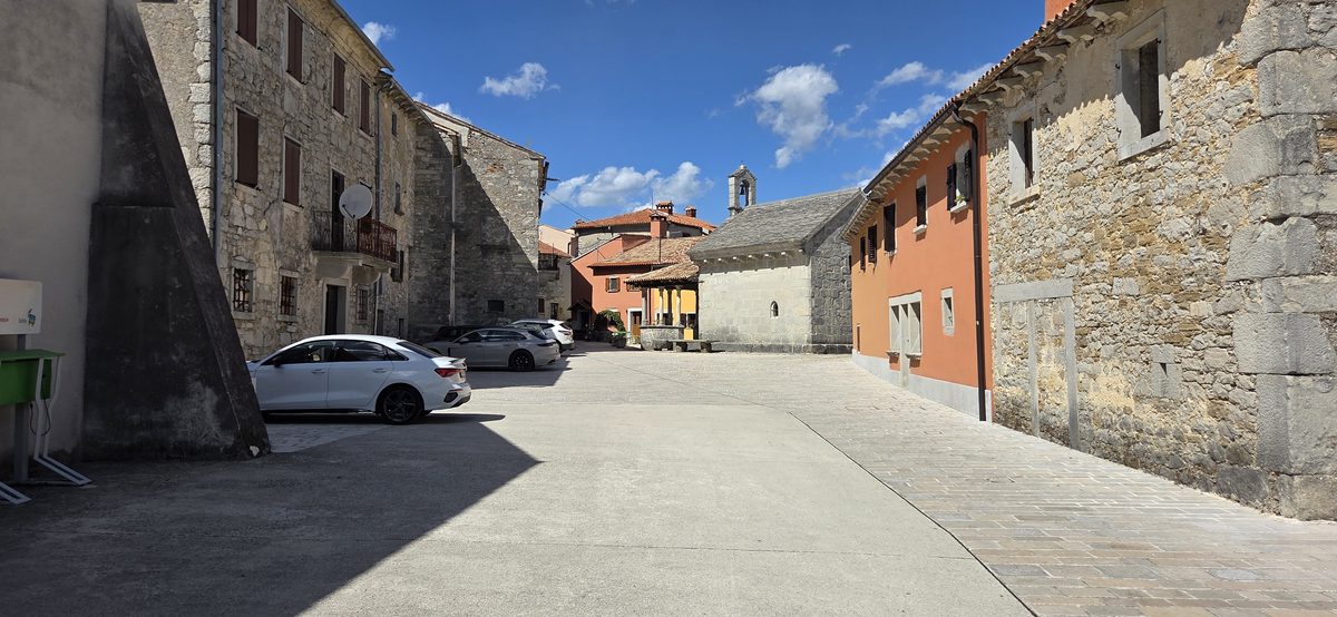 Steinhäuser und geparkte Autos an einer Dorfstraße in Gračišće
